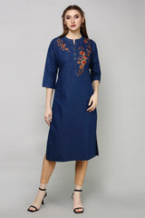 A woman modeling a dark blue cotton kurta with orange and red floral embroidery on the chest, paired with beige leggings and black sandals, against a solid gray studio background.