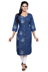 A woman modeling a blue denim-style kurta with white embroidered motifs and a button-front placket, paired with white pants and black sandals, against a plain white background.
