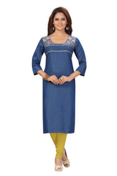 A woman modeling a blue denim-style straight kurta with colorful floral embroidery around the neckline, paired with mustard yellow leggings and beige heels, against a plain white background.