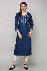 A woman modeling a dark blue cotton kurta with white embroidery on the chest and cuffs, paired with white leggings and black shoes, against a plain gray studio background.
