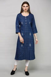 A woman modeling a dark blue plaid kurta with white embroidered motifs, paired with white leggings and black slip-on shoes, against a solid gray studio background.