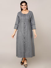A woman modeling a long gray button-front tunic dress with three-quarter sleeves and subtle vertical pleating details, photographed against a plain light gray studio background.