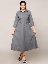 A woman modeling a gray denim midi shirt dress with three-quarter sleeves, a button-down front, and side pockets, paired with black strappy heels against a solid beige studio background.