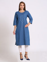 A woman modeling a blue cotton kurta with white embroidered details on the chest, paired with white leggings and navy blue heels, against a plain light gray background.