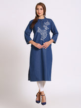 A woman modeling a blue cotton kurta with white floral embroidery on the chest, paired with white leggings and navy blue heels, against a light gray studio background.