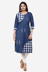 A woman modeling a blue denim-style tunic dress with white and navy gingham check panels on the chest and lower hem, white embroidered details, white tights, and tan heeled sandals against a light gray background.