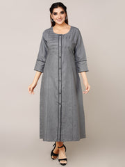 A woman modeling a long gray button-front tunic dress with three-quarter sleeves and subtle vertical pleating details, photographed against a plain light gray studio background.