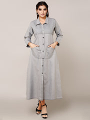 A woman modeling a light gray denim maxi shirt dress with a button-down front, collar, and front pockets, standing against a solid beige studio background.