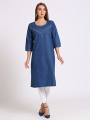 A woman modeling a blue cotton kurta with three-quarter sleeves, a round neckline, and a buttoned chest panel with decorative stitching, paired with white leggings and navy heels, against a light gray studio background.