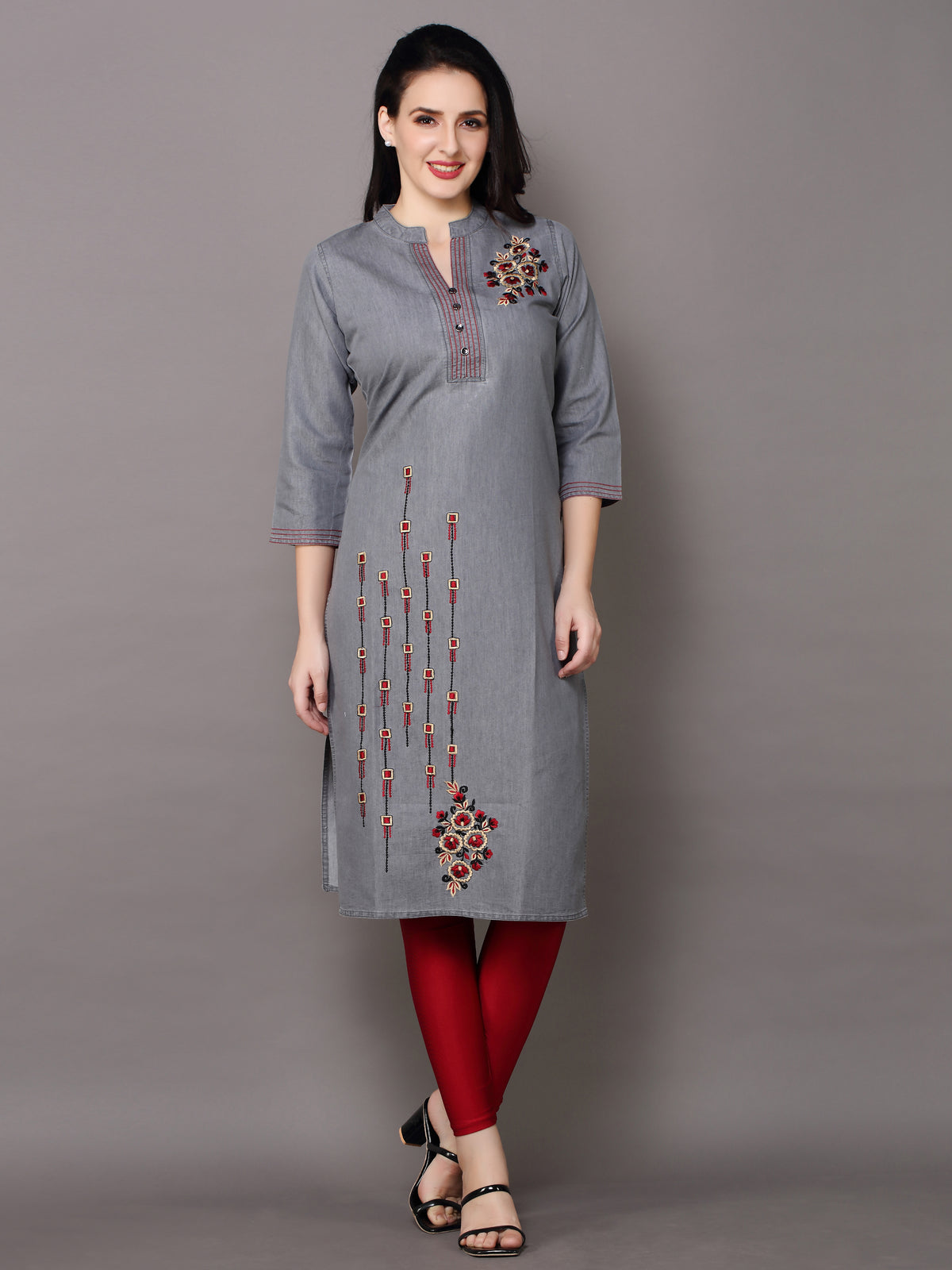 A woman modeling a gray three-quarter sleeve kurta with red and gold embroidered details, paired with red leggings and black sandals, against a solid gray studio background.