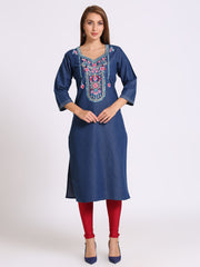A woman modeling a blue denim-style kurta with colorful floral embroidery around the neckline, paired with red leggings and navy heels, against a plain light gray studio background.