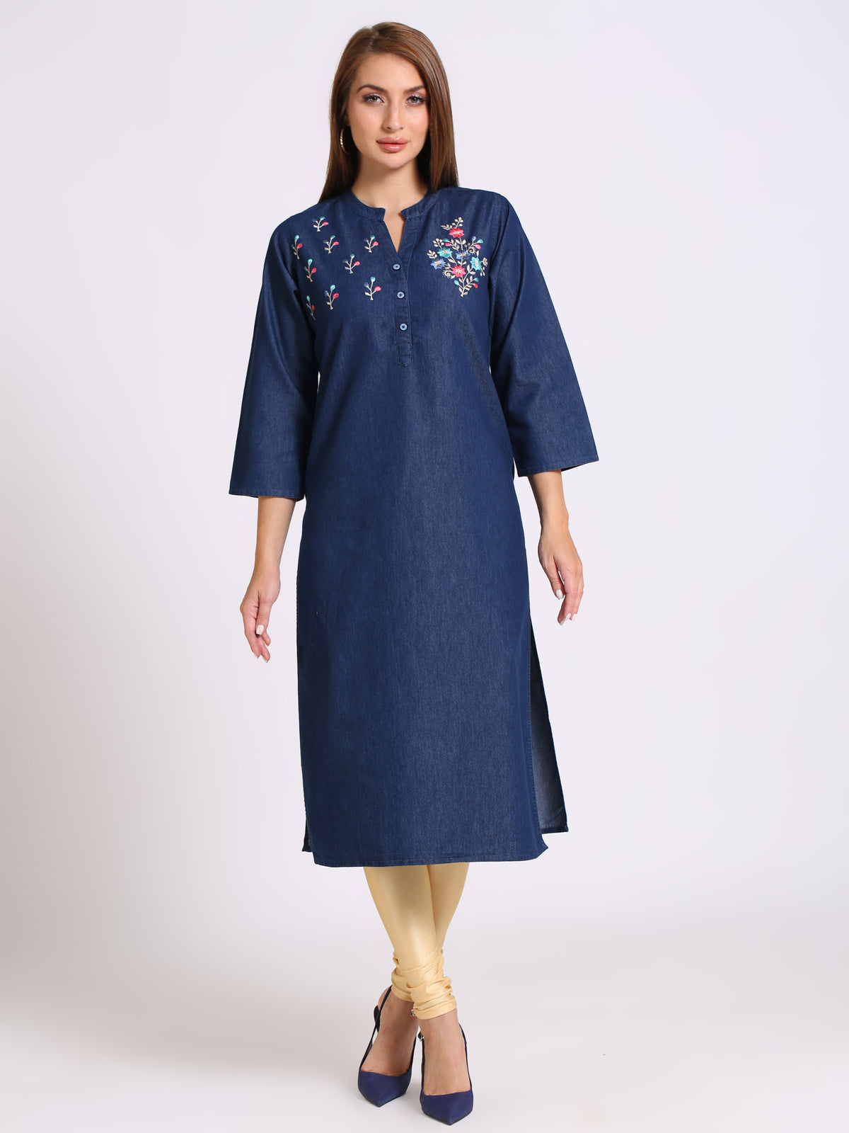 A woman modeling a navy blue cotton kurta with colorful floral embroidery on the chest, paired with beige leggings and navy blue heels, against a plain light gray background.