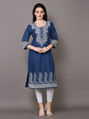 A woman modeling a navy blue kurta with intricate white embroidery on the neckline, sleeves, and hem, paired with white leggings and white heeled sandals against a solid gray studio background.