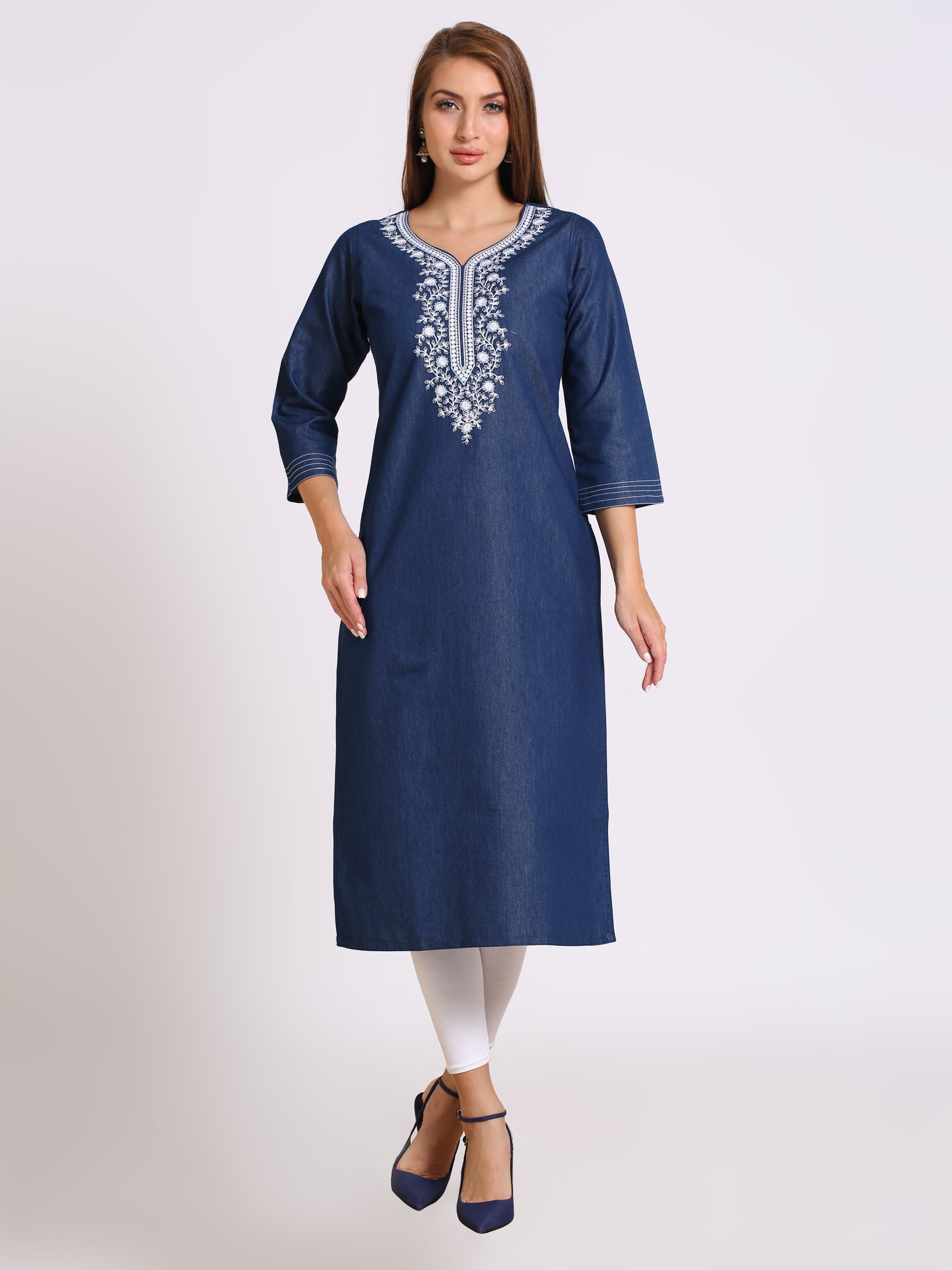 A woman modeling a navy blue cotton kurta with white embroidery around the neckline, paired with white leggings and navy blue heels, against a light gray studio background.
