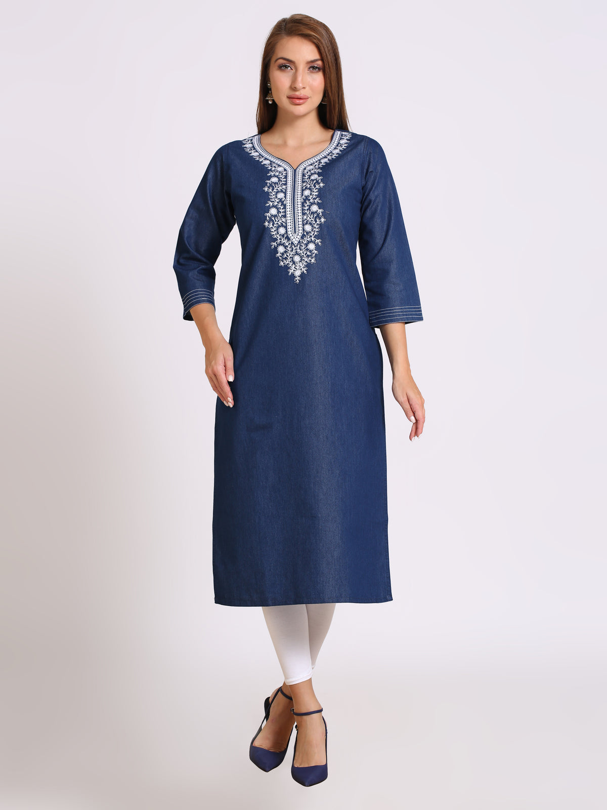 A woman modeling a navy blue cotton kurta with white embroidery around the neckline, paired with white leggings and navy blue heels, against a light gray studio background.