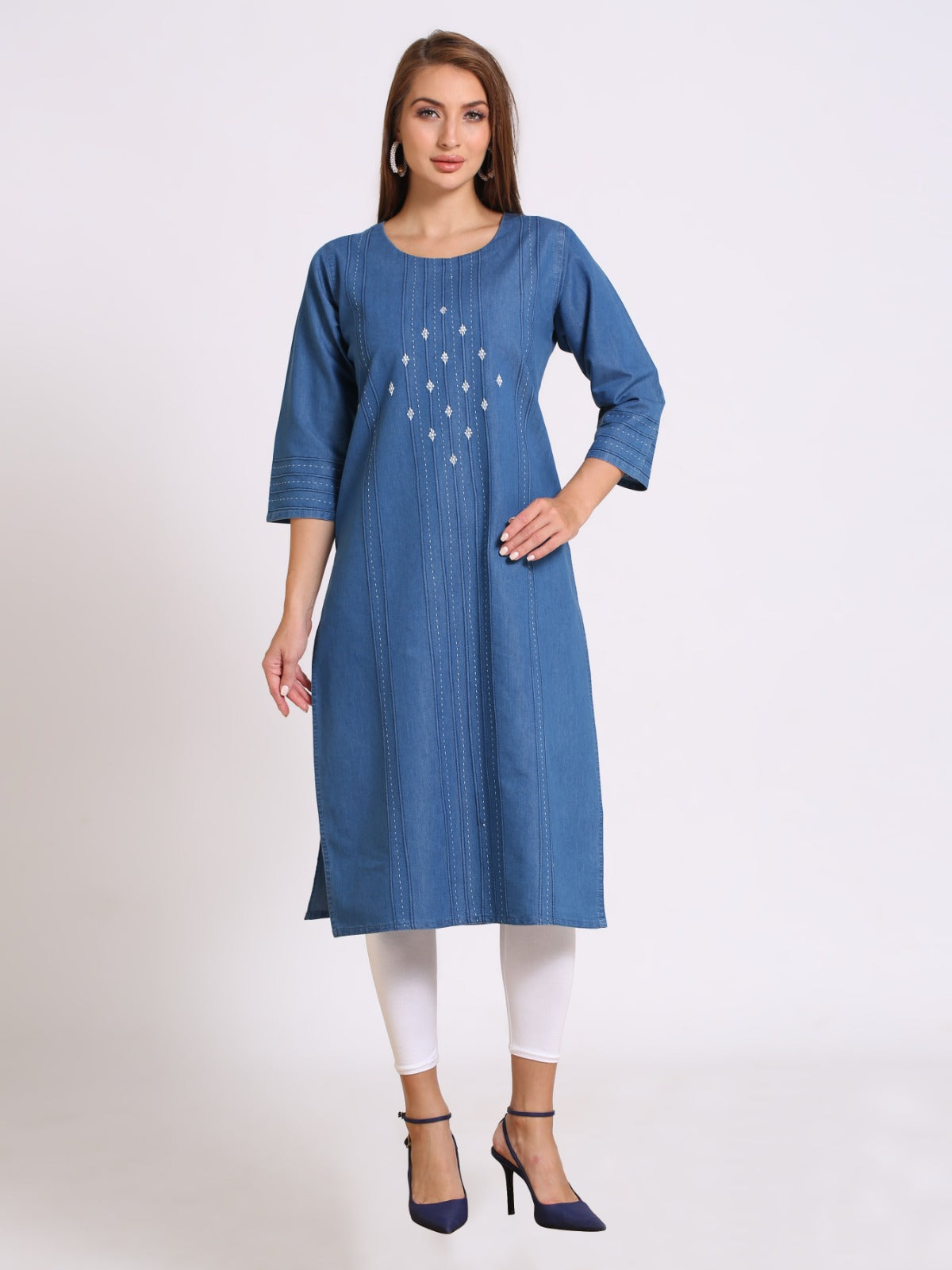 A woman modeling a blue cotton kurta with white embroidered details on the chest, paired with white leggings and navy blue heels, against a plain light gray background.