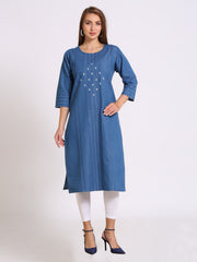A woman modeling a blue cotton kurta with white embroidered details on the chest, paired with white leggings and navy blue heels, against a plain light gray background.
