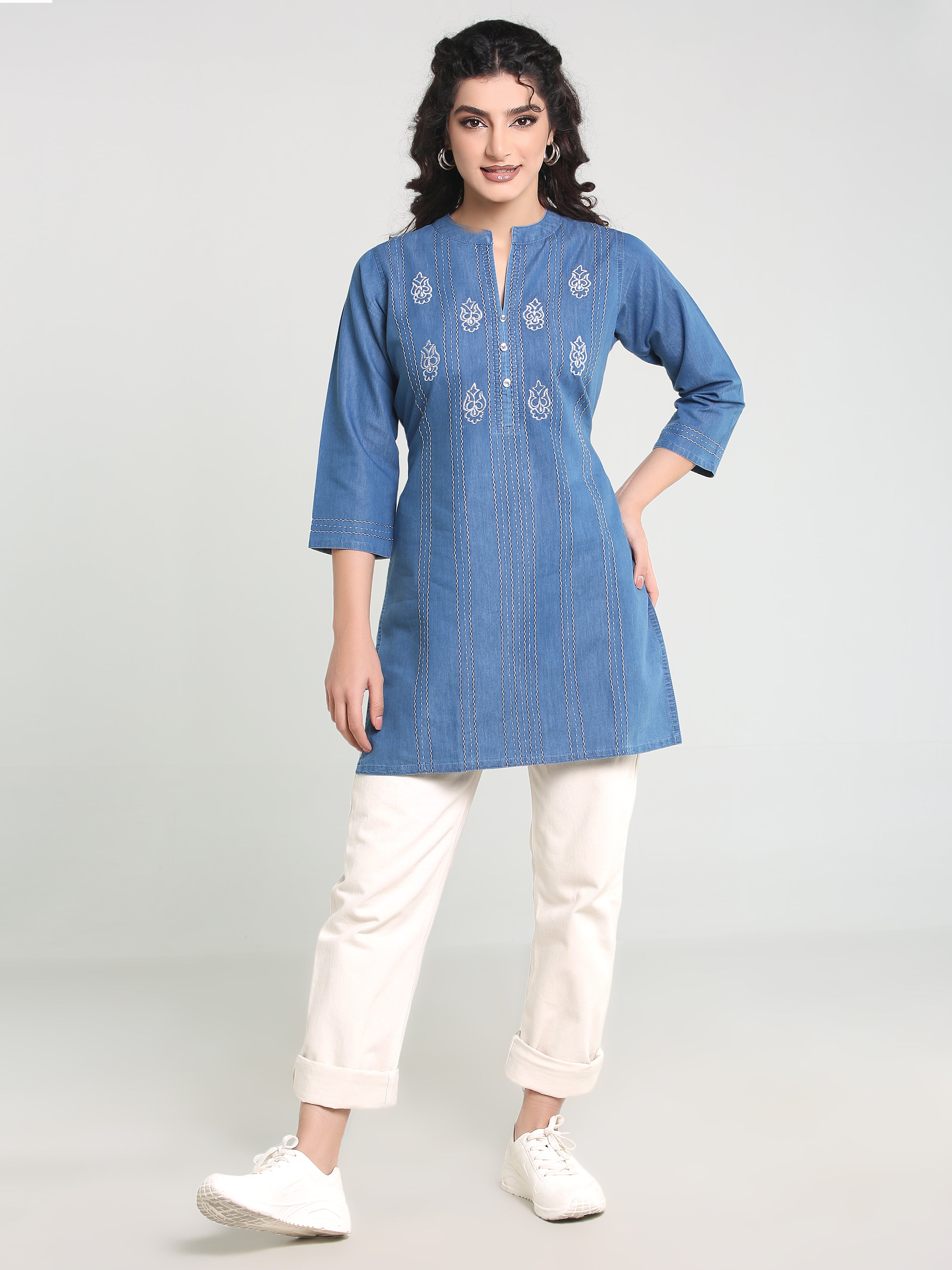 Woman wearing a blue embroidered kurta with white pants on a light gray background